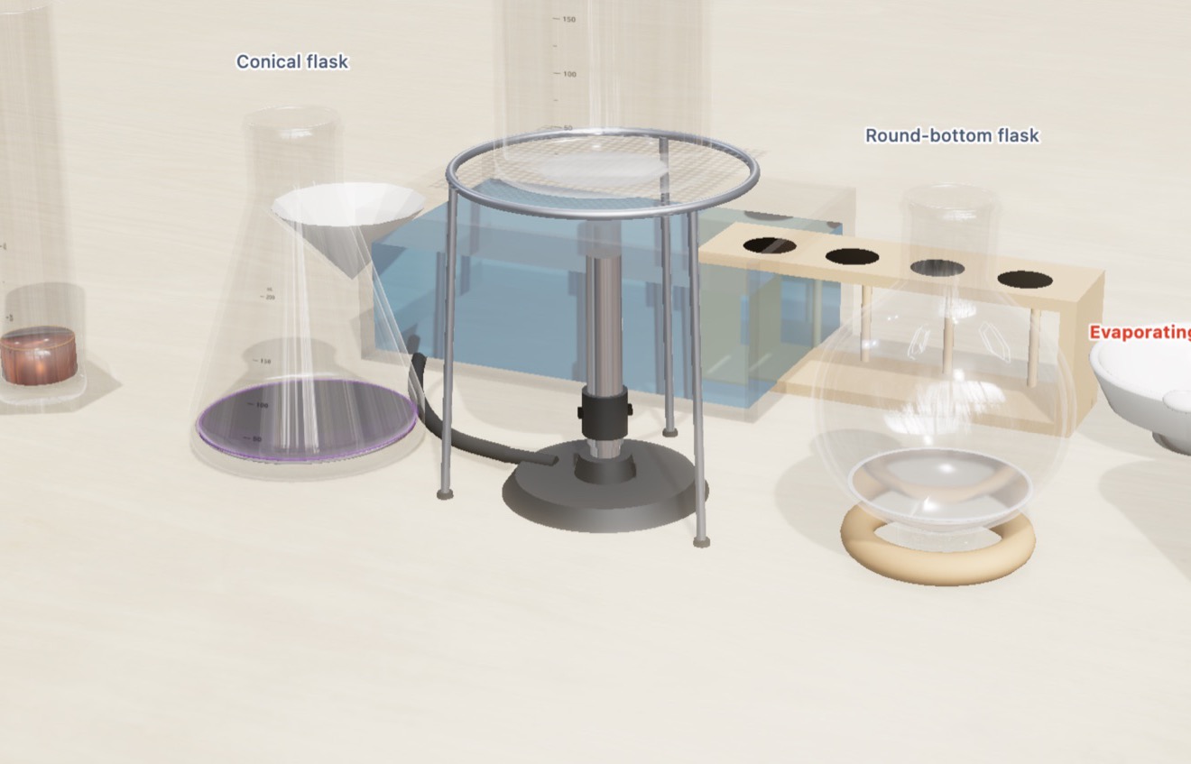 The Chemistry Lab table: permanganate in a conical flask, iron(III) chloride in a measuring cylinder, a round bottom flask in its ring, a trough, a rack, a funnel and a lit Bunsen burner on a birch bench